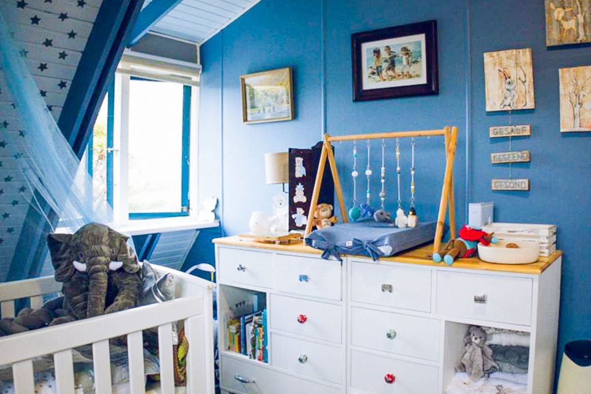 A cozy bedroom featuring a sloped ceiling and a casement window, finished with blue wall paneling.