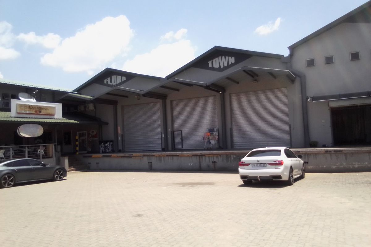 Commercial warehouse facility featuring multiple roller shutter doors, a raised loading dock, and a paved yard area.