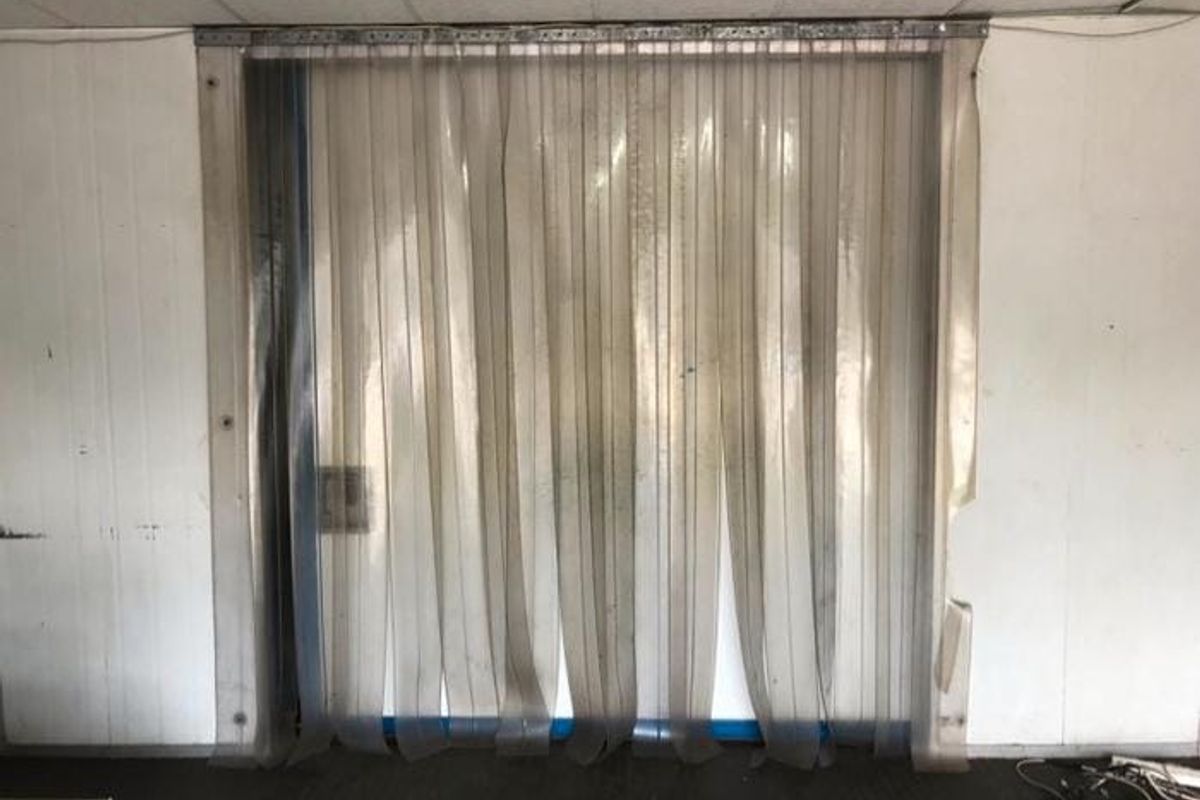 Utility space featuring industrial PVC strip curtains, suspended ceiling, and panelled wall finishes, suitable for storage or commercial prep area.