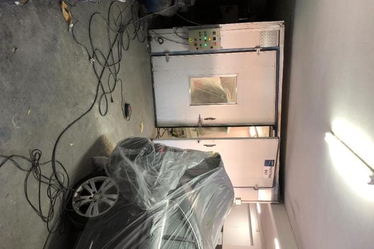 Commercial utility space featuring a dedicated industrial spray booth with integrated control panel and overhead fluorescent lighting.