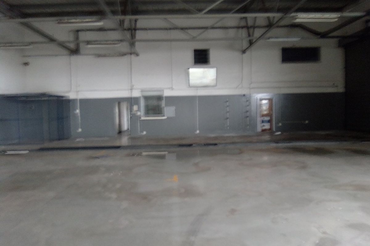A large, open-plan industrial utility space featuring exposed steel roof trusses, concrete flooring, and functional internal access points.