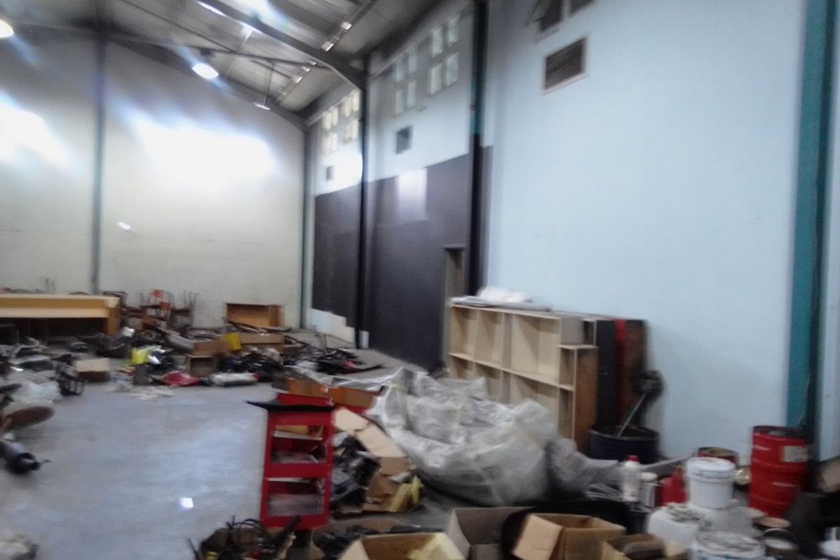 A large commercial utility or warehouse space featuring high ceilings, exposed steel structural elements, and concrete flooring, currently used for storage.