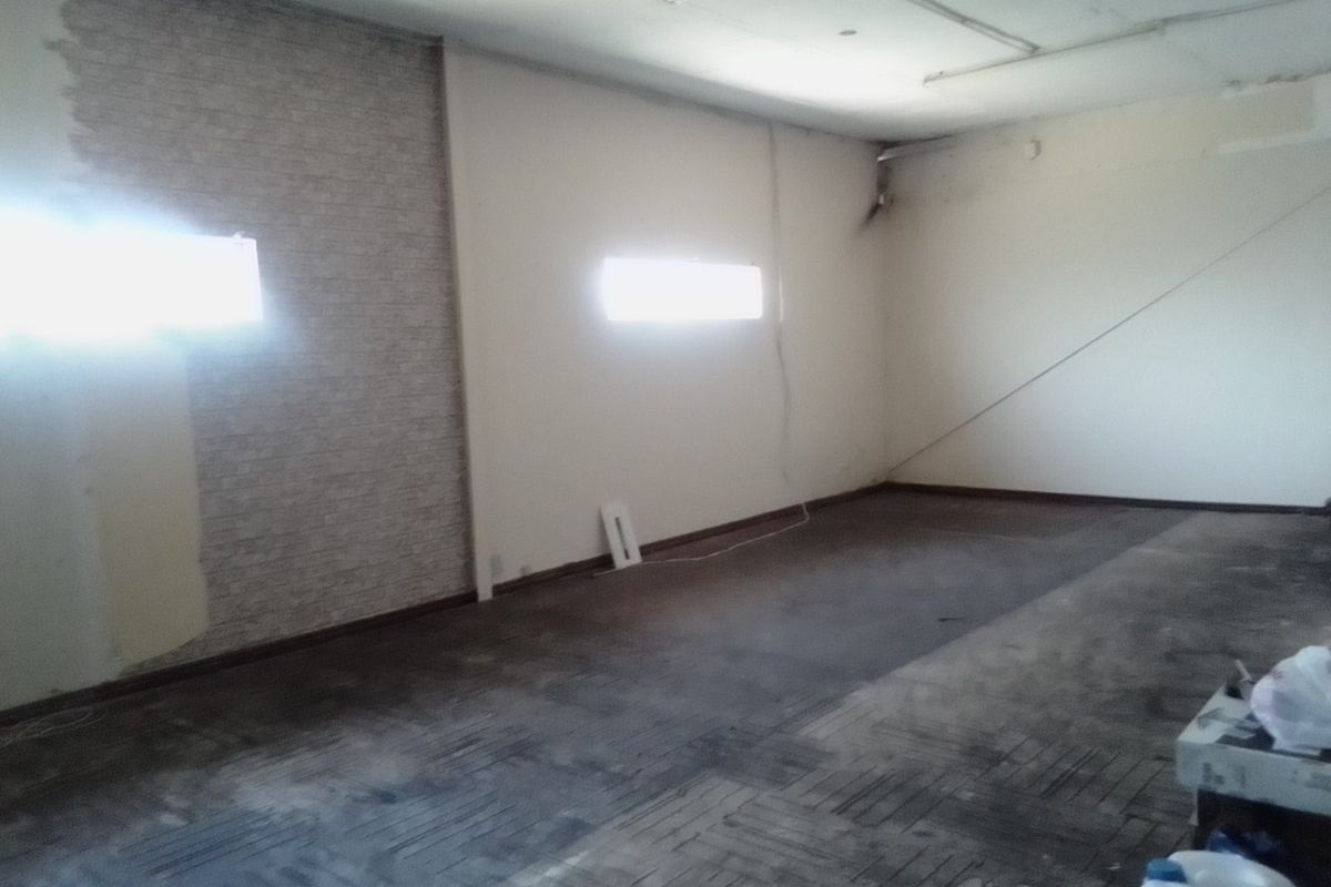 An empty, open-plan commercial space featuring high-level windows, exposed brickwork, and worn flooring, requiring significant refurbishment to restore its functional condition.