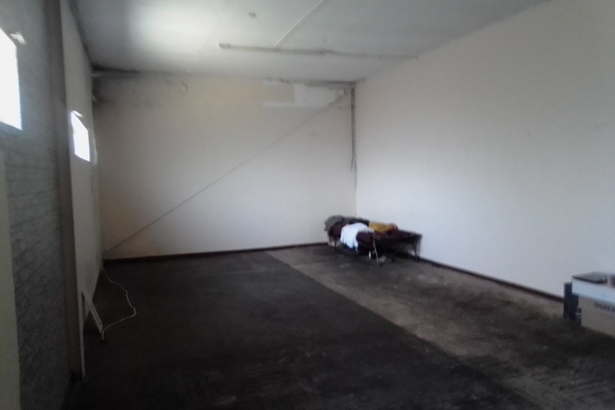A vacant commercial utility space featuring exposed ceiling, basic lighting, and worn flooring, suitable for renovation or storage.
