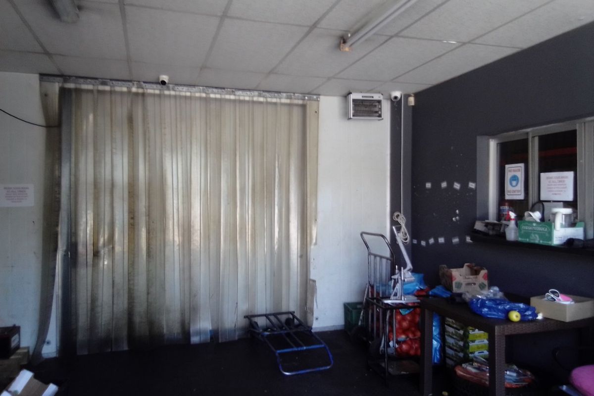 A functional utility or storage area featuring a plastic strip curtain, suspended ceiling, and a service window, suitable for commercial operations.
