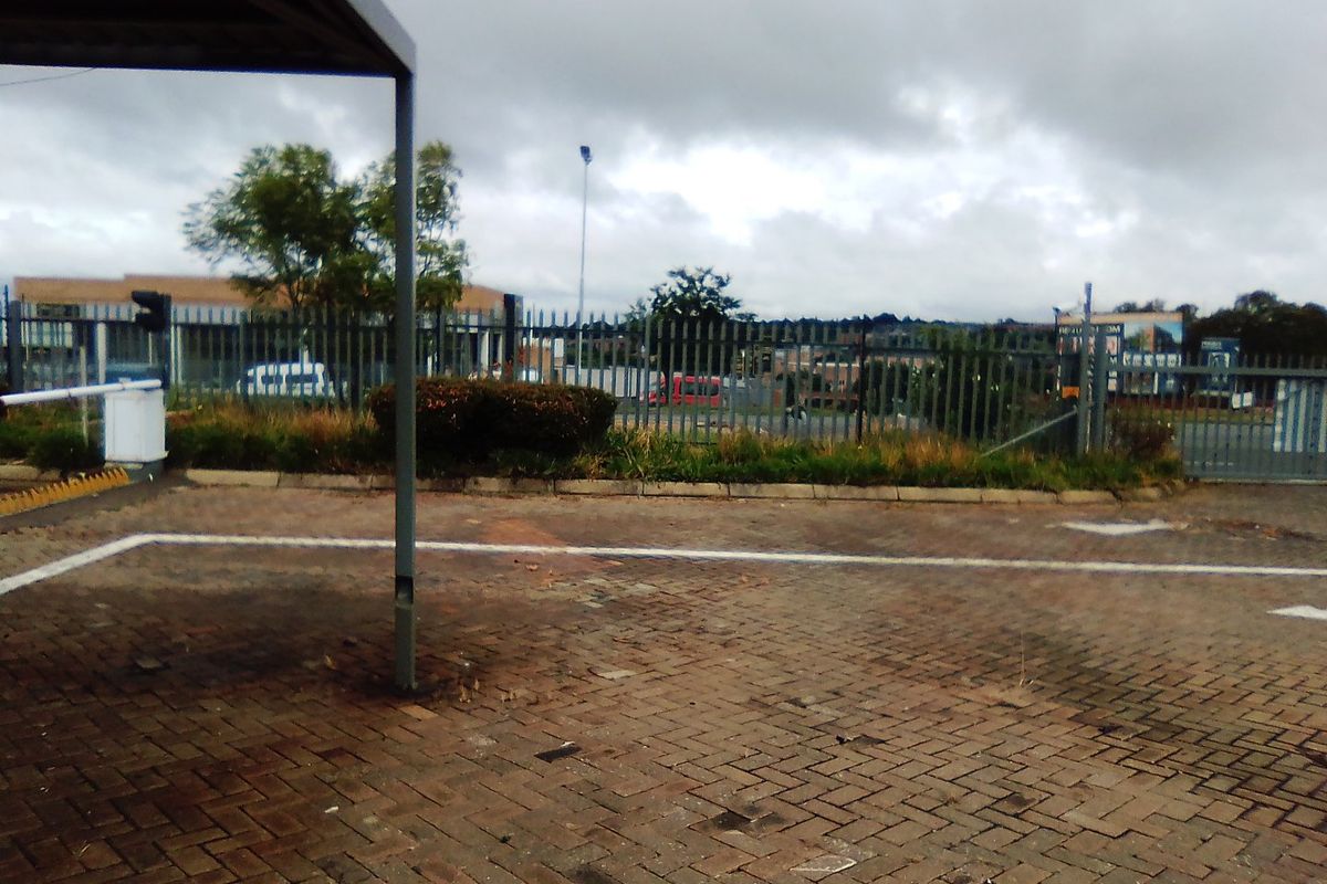 Commercial exterior area featuring a paved driveway, carport structure, and perimeter security fencing.