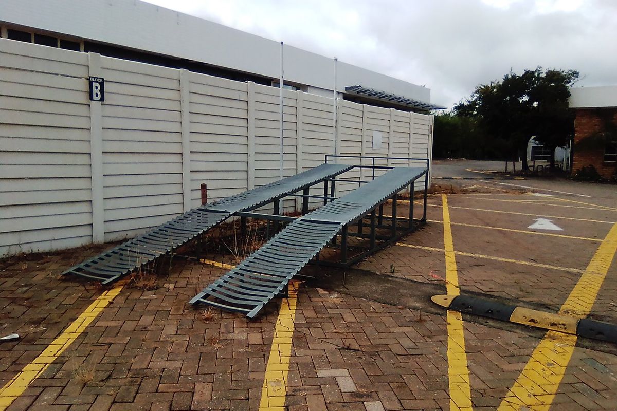 Exterior view of a commercial property rear area featuring paved parking, a precast boundary wall, and a metal loading ramp.