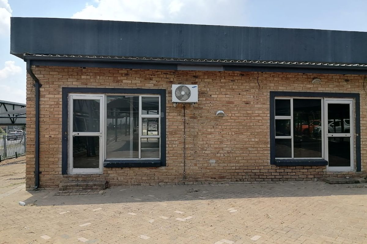 Exterior view of a commercial building featuring a face brick facade, aluminium window and door frames, and a wall-mounted air conditioning unit.