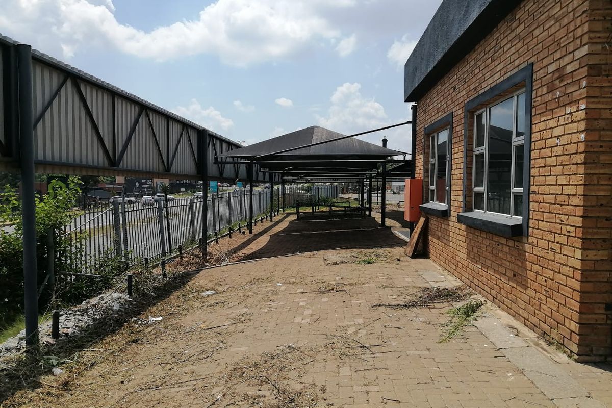 Exterior rear view of a commercial property featuring a paved walkway, metal shade structure, and brick facade with aluminum windows.