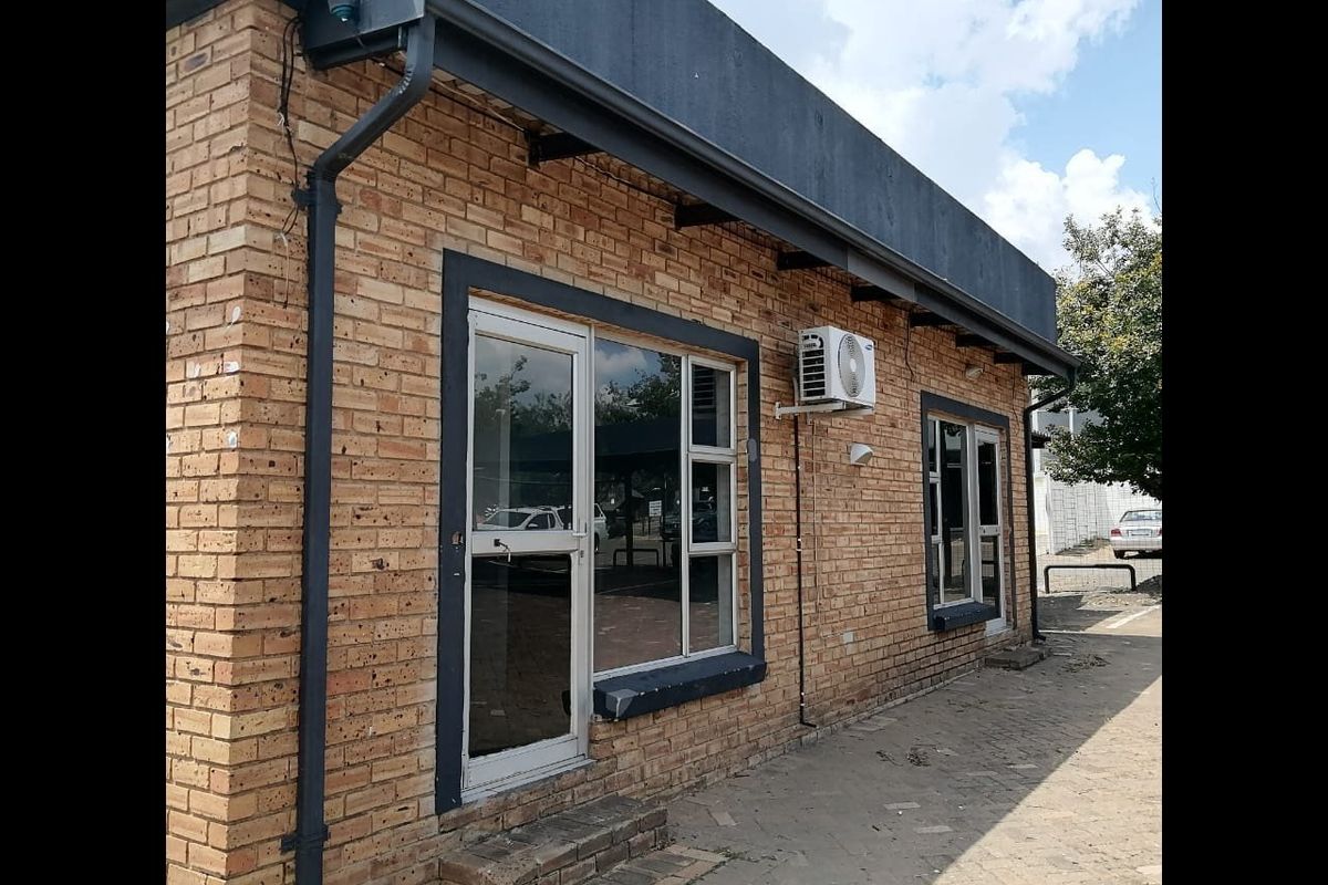 Exterior view of a commercial building featuring face brick construction, aluminium framed windows and doors, and an external air conditioning unit.