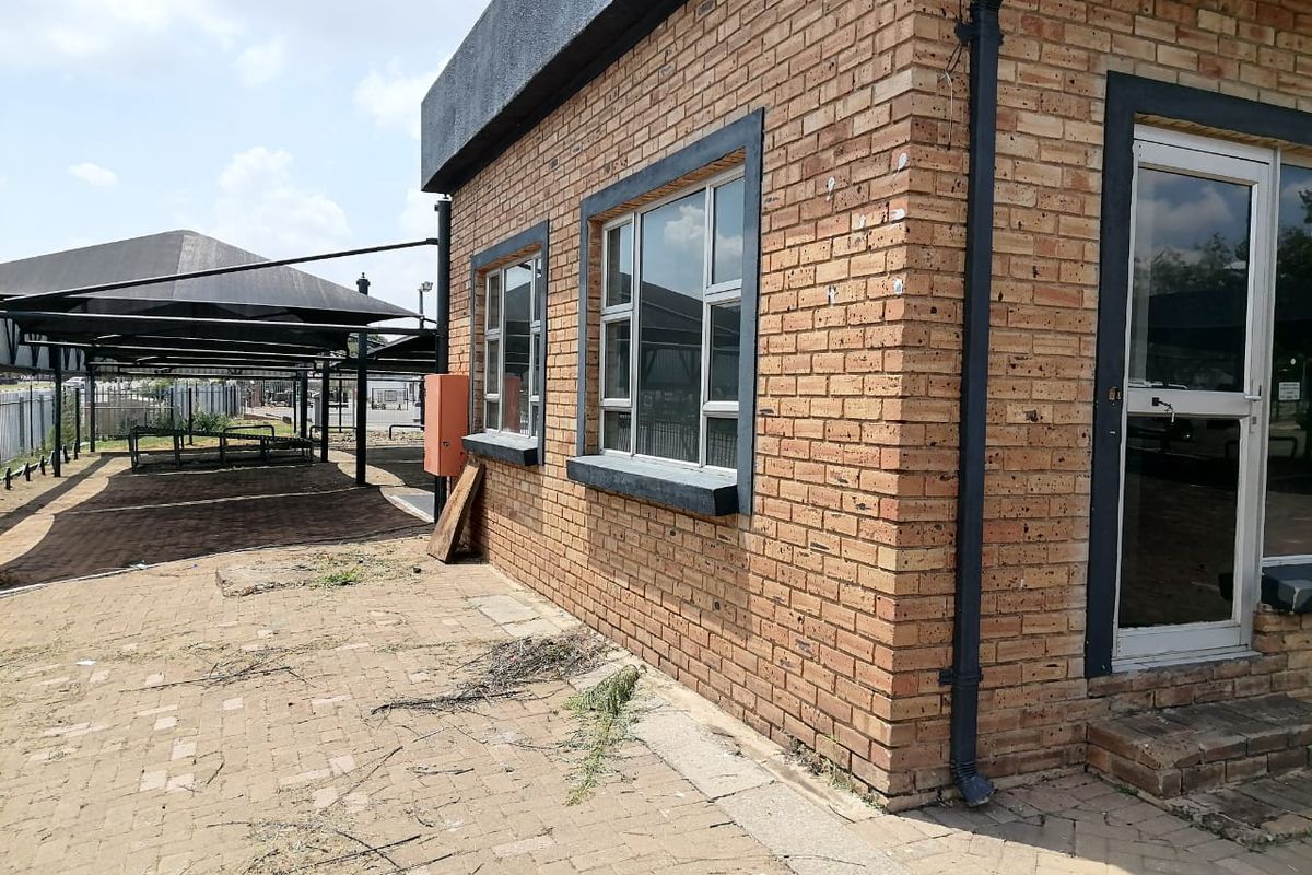Exterior view of a commercial face brick building featuring aluminium windows, a glass entrance door, and an adjacent shade cloth carport area.