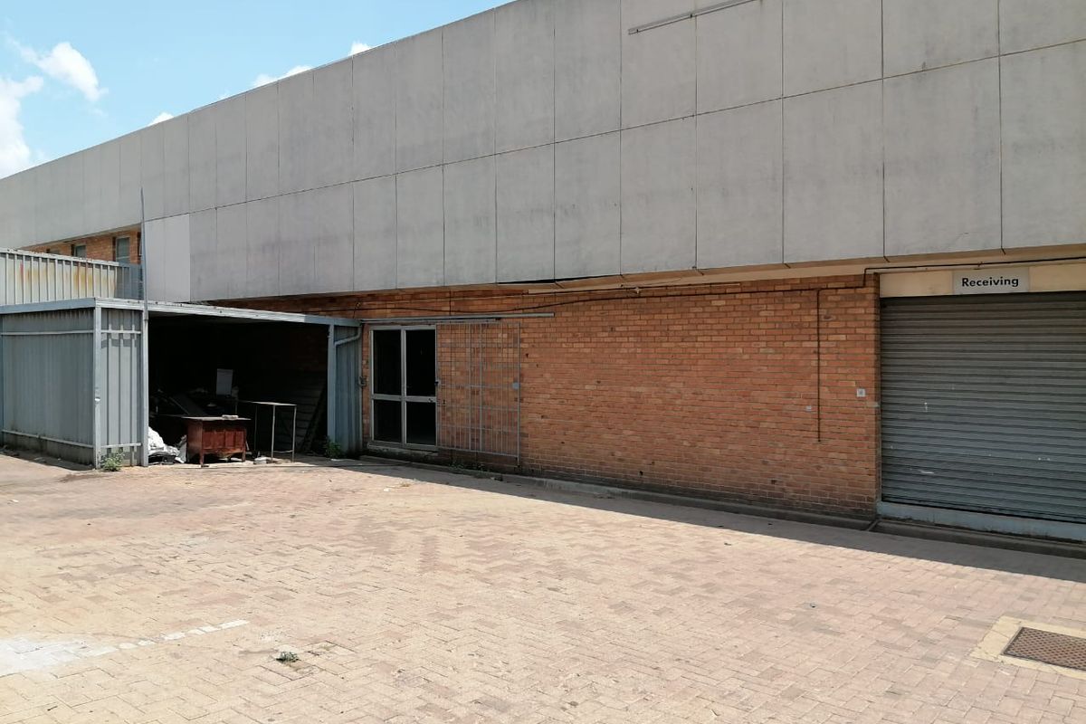 Rear industrial exterior featuring a paved yard, roller shutter receiving door, and brick facade with metal canopy structure.