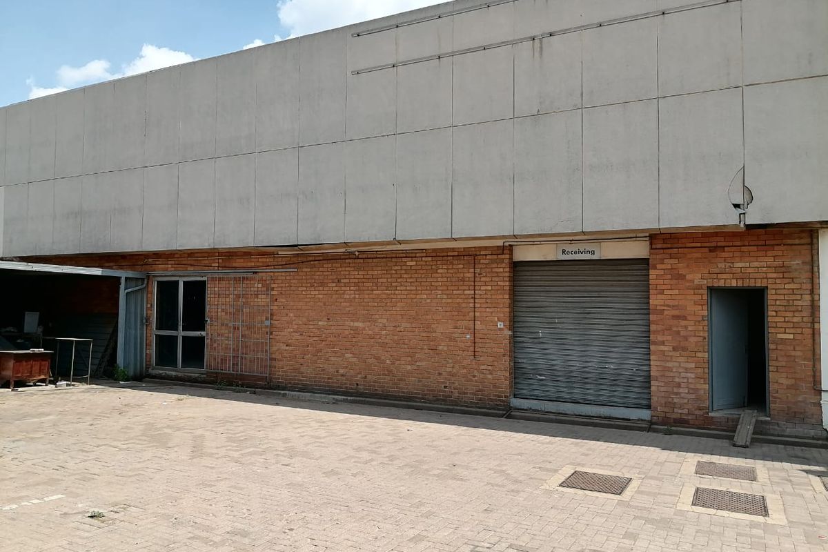 Industrial rear exterior featuring a brick facade, concrete cladding, a roller shutter receiving door, and a paved yard area.