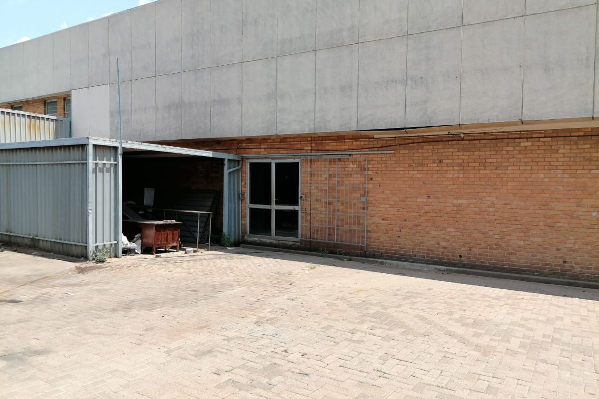 Rear exterior view of an industrial property featuring a brick and concrete facade, paved yard area, and a metal lean-to structure.