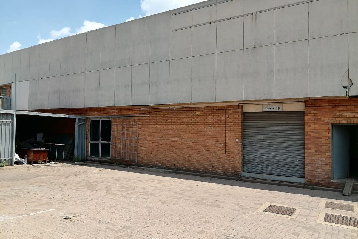Rear industrial exterior featuring a brick facade, concrete panel cladding, and a dedicated receiving area with a roller shutter door.