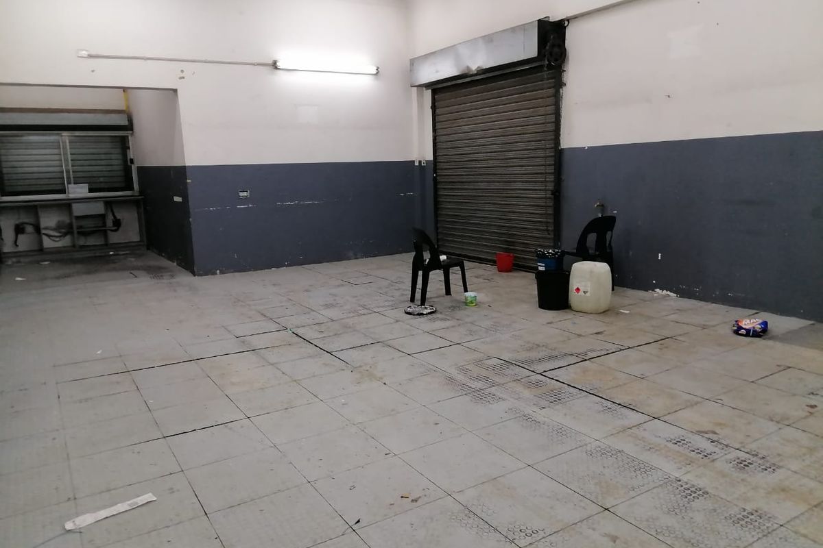 An industrial utility space featuring tiled flooring, a roller shutter door, and a service hatch, suitable for storage or workshop use.