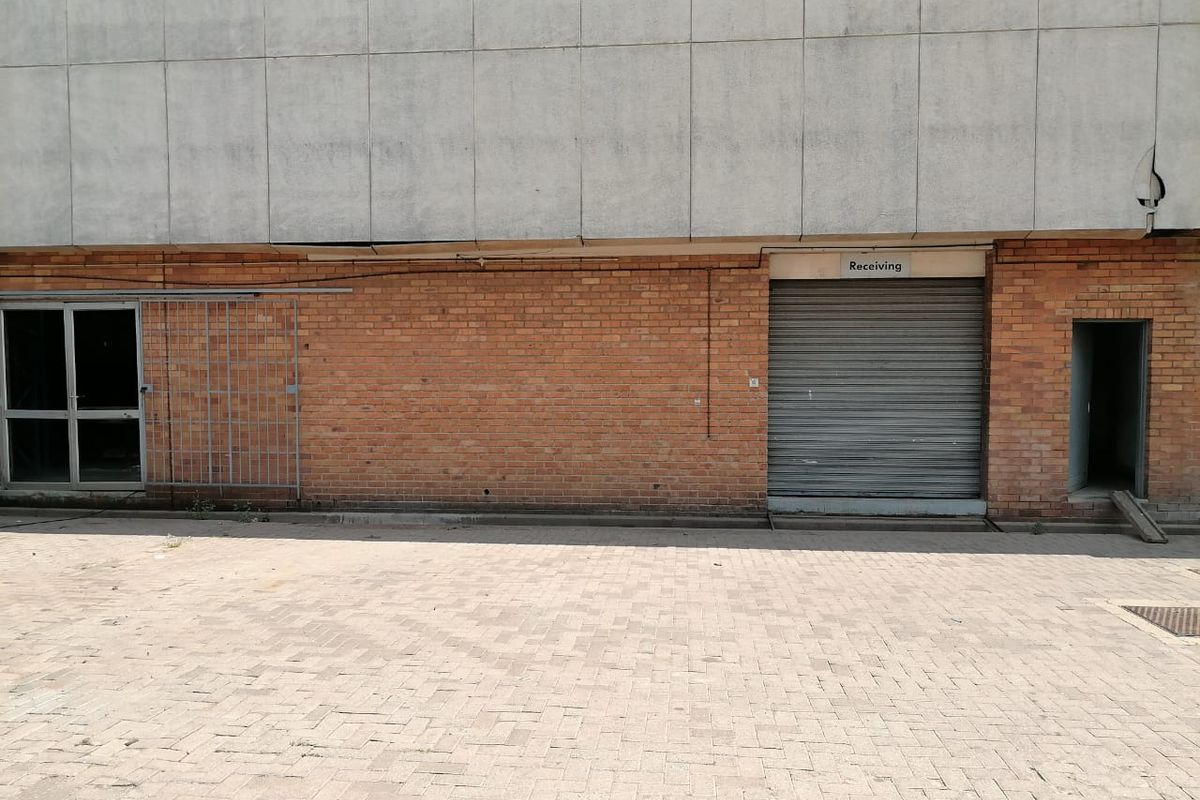 Industrial rear exterior featuring a brick facade, roller shutter receiving door, security gate, and paved yard area.