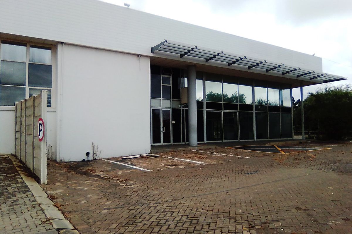 Front exterior view of a commercial building featuring a glass facade, metal awning, and paved parking area.
