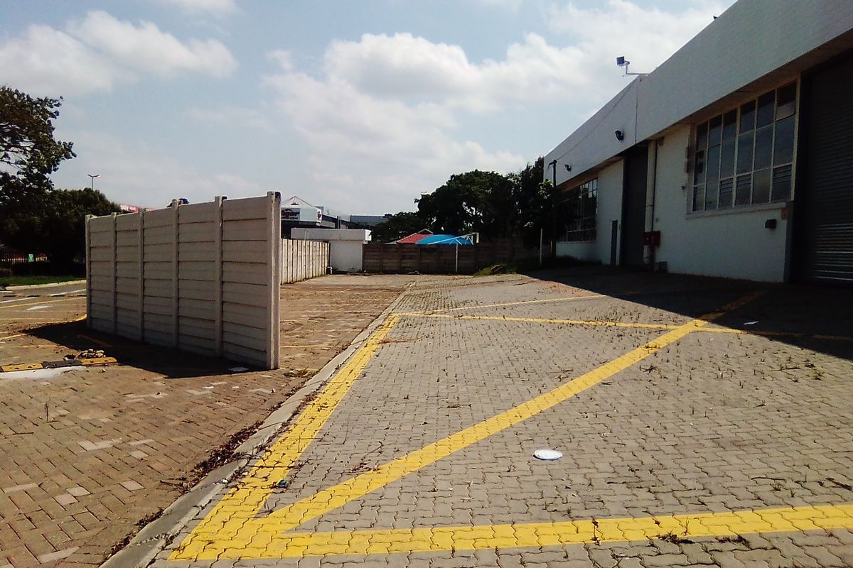 Rear exterior view of a commercial property featuring a paved parking area, boundary wall, and roller shutter access.