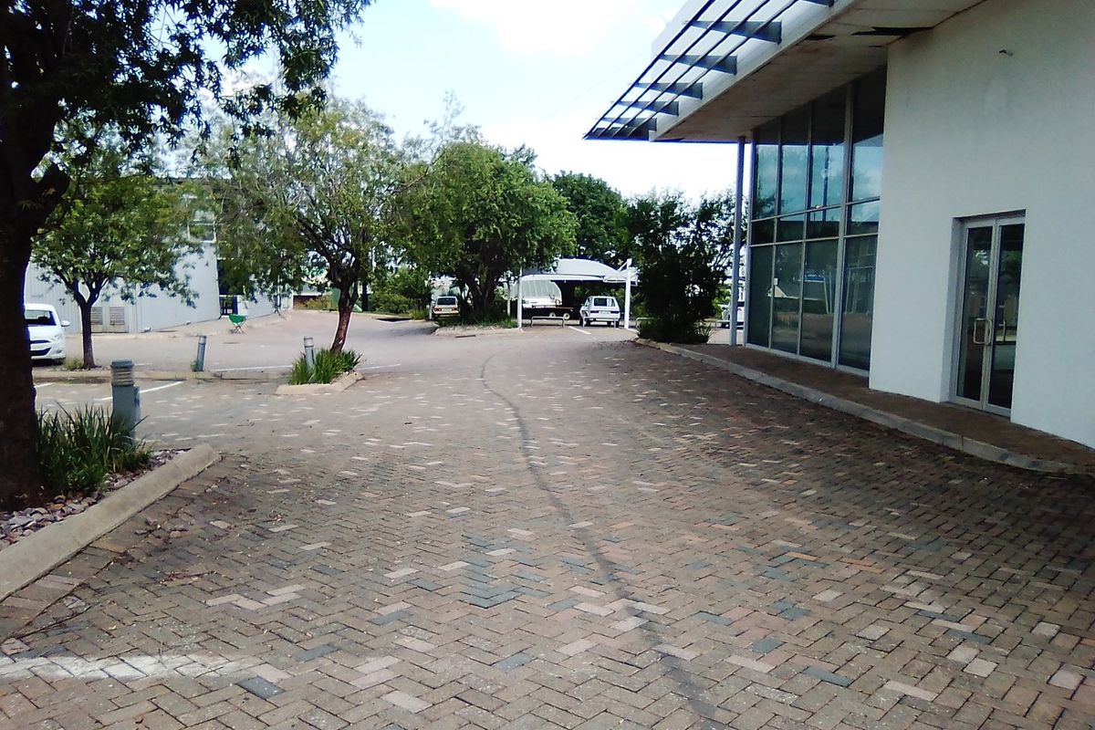 Commercial property exterior featuring a paved driveway, glass facade, and metal awning structure.