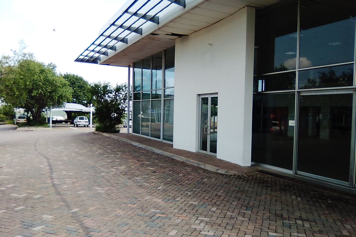 Commercial building exterior featuring a glass facade, metal roof overhang, and paved driveway entrance.
