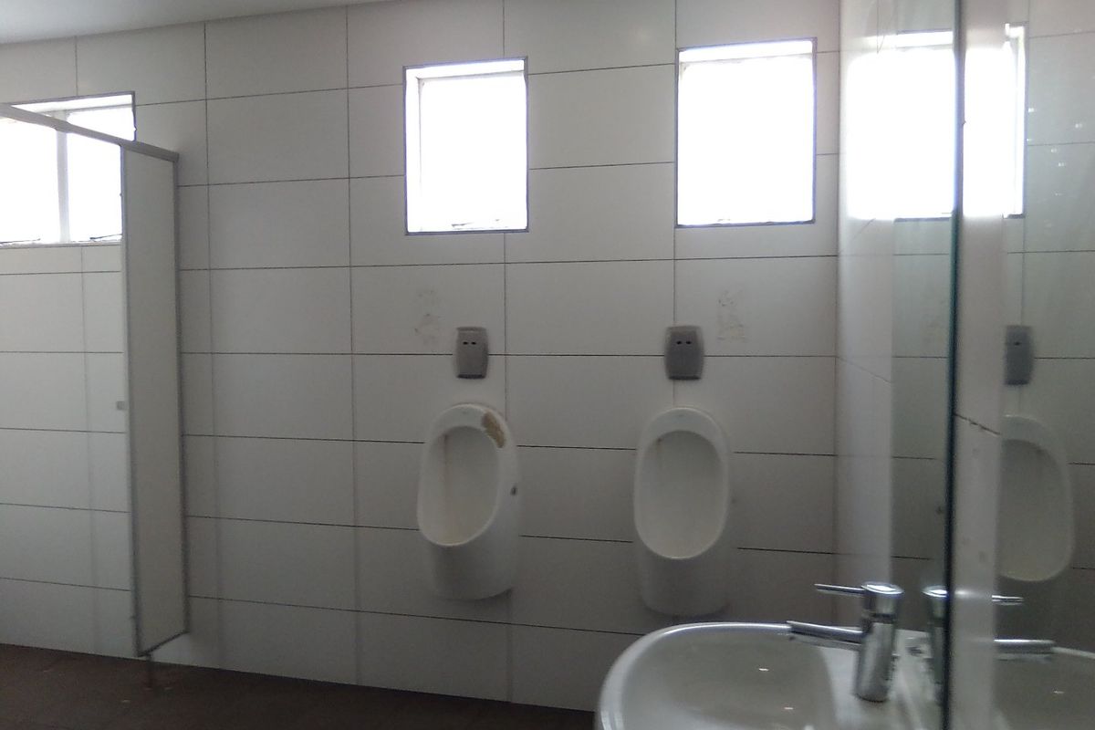 Commercial bathroom facility featuring wall-mounted urinals, a pedestal washbasin with chrome fixtures, and tiled wall finishes.