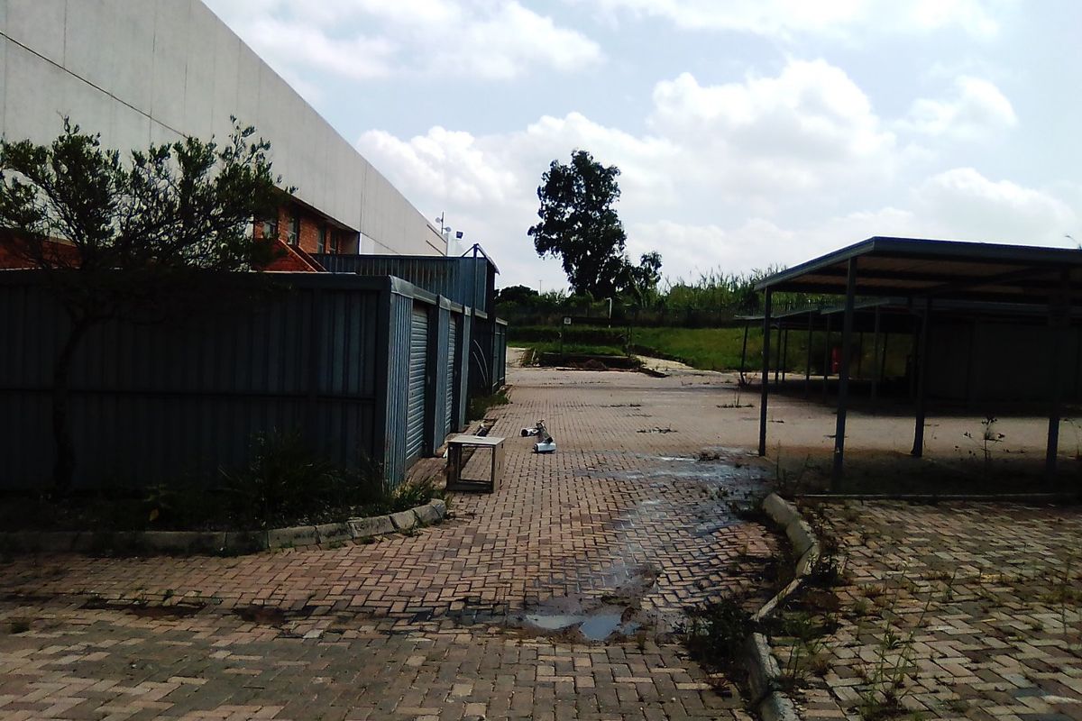 Rear exterior area featuring paved driveway, metal storage units, and a covered parking structure, showing signs of wear and maintenance requirements.
