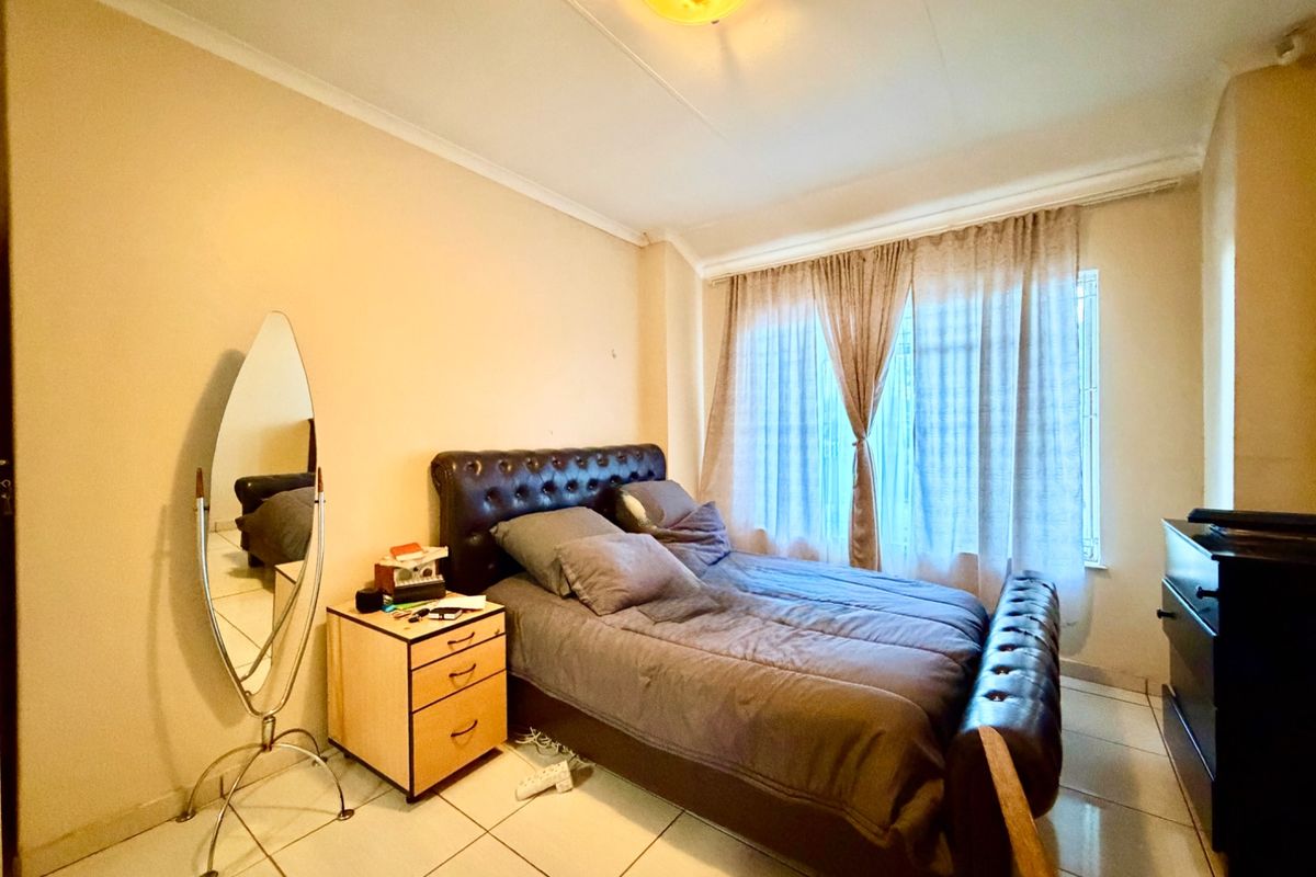 A bedroom featuring tiled flooring, a window with security bars, and a central ceiling light fixture.