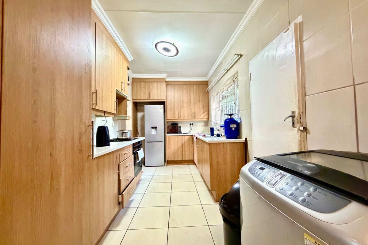 A functional galley-style kitchen featuring extensive wooden cabinetry, tiled surfaces, and integrated cooking appliances, offering a practical layout for daily meal preparation.