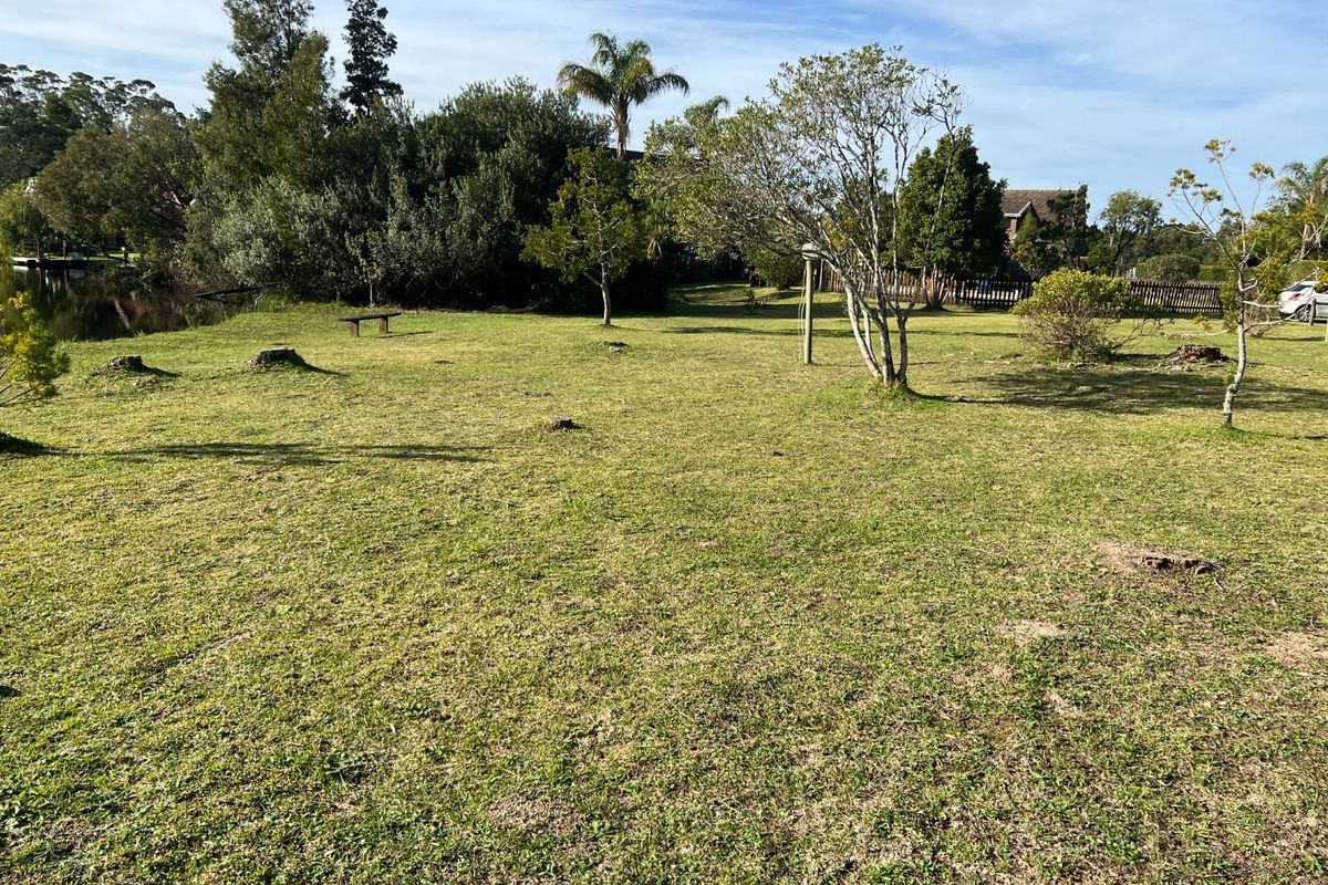 A spacious, grassy residential plot featuring mature trees and direct waterfront access, offering a peaceful and natural setting.