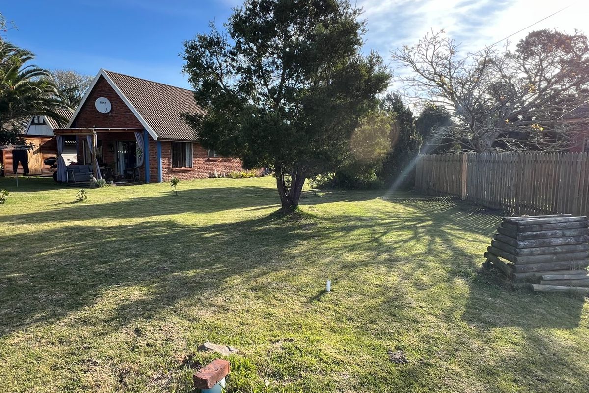 A view of the rear garden featuring a brick residential dwelling with a tiled roof, a covered patio area, and a wooden perimeter fence.