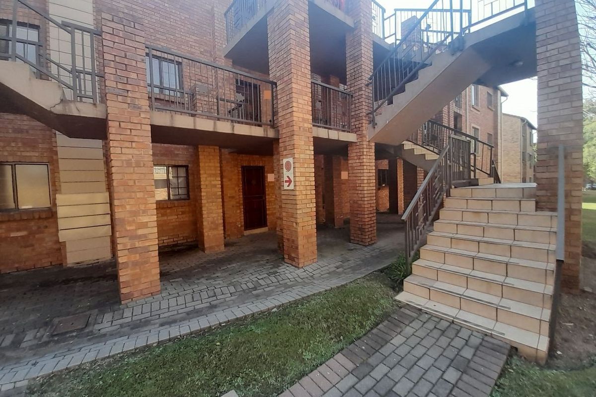 Exterior view of a multi-story apartment complex featuring exposed brickwork, external metal staircases, and paved walkways.