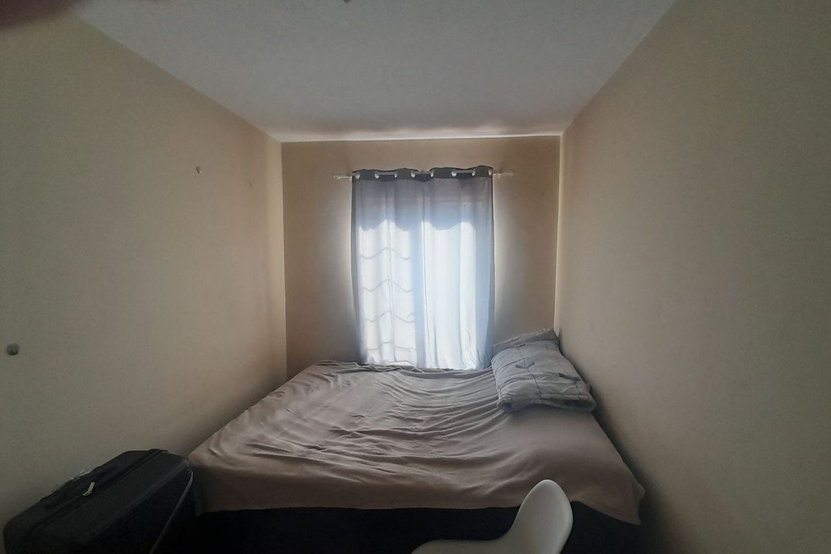 A compact bedroom featuring neutral walls and a window with installed curtain rod, providing a functional space for rest.
