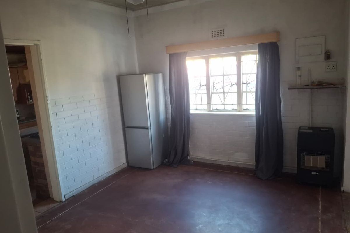 An empty living area featuring exposed brick walls, concrete flooring, and security bars on the window, requiring cosmetic updates and renovation.