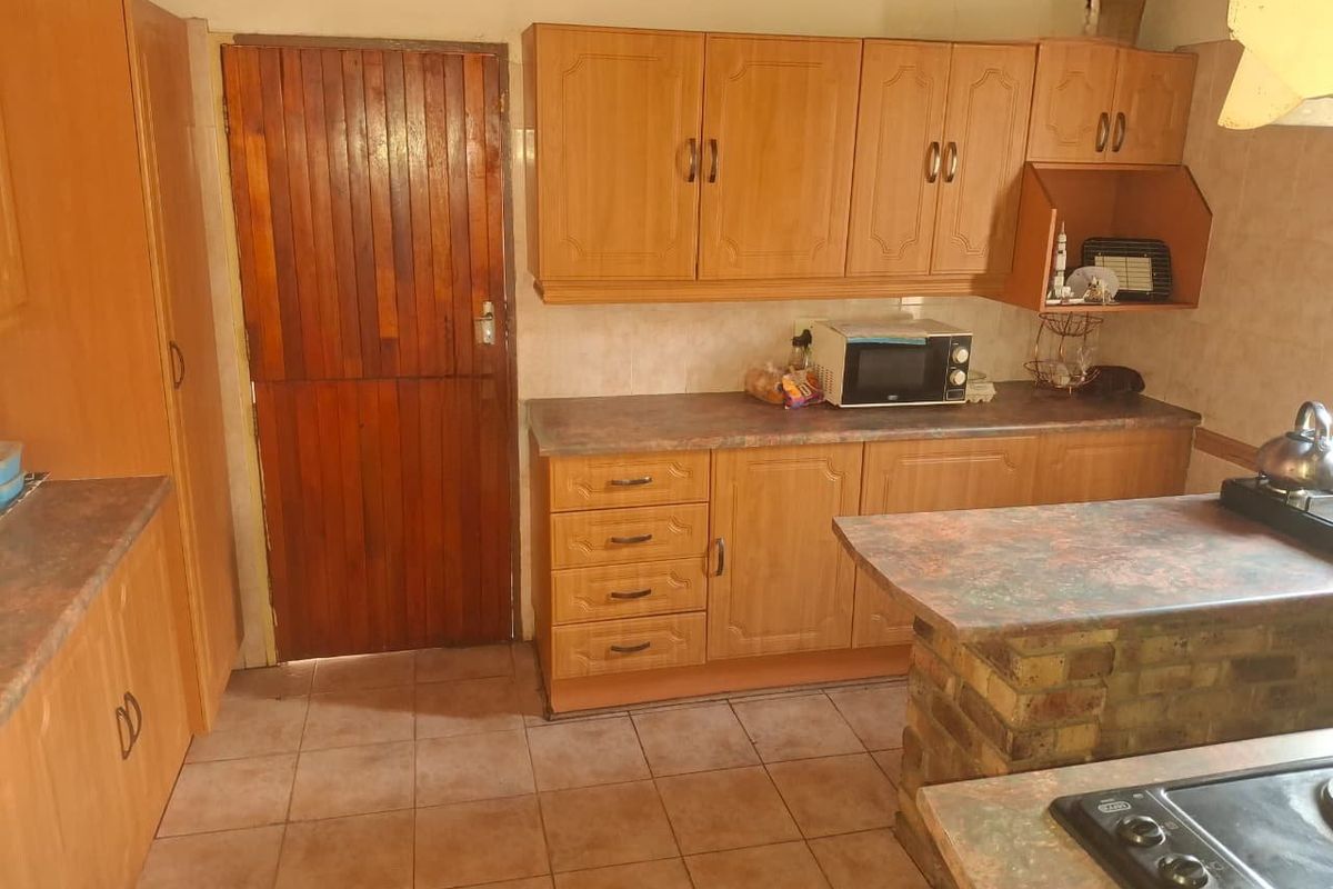 A functional kitchen featuring timber cabinetry, laminate countertops, a brick breakfast bar, and ceramic floor tiles, offering a traditional layout with potential for modernization.