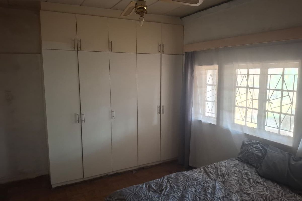 Bedroom featuring built-in cupboards, a ceiling fan, and parquet flooring, with security bars installed on the windows.