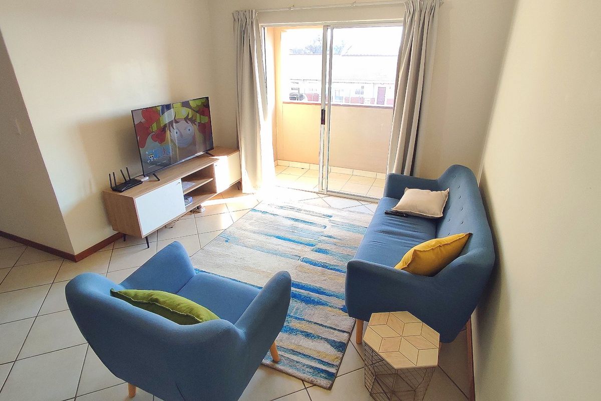 A bright living room featuring tiled flooring and a sliding glass door providing access to an outdoor balcony area.