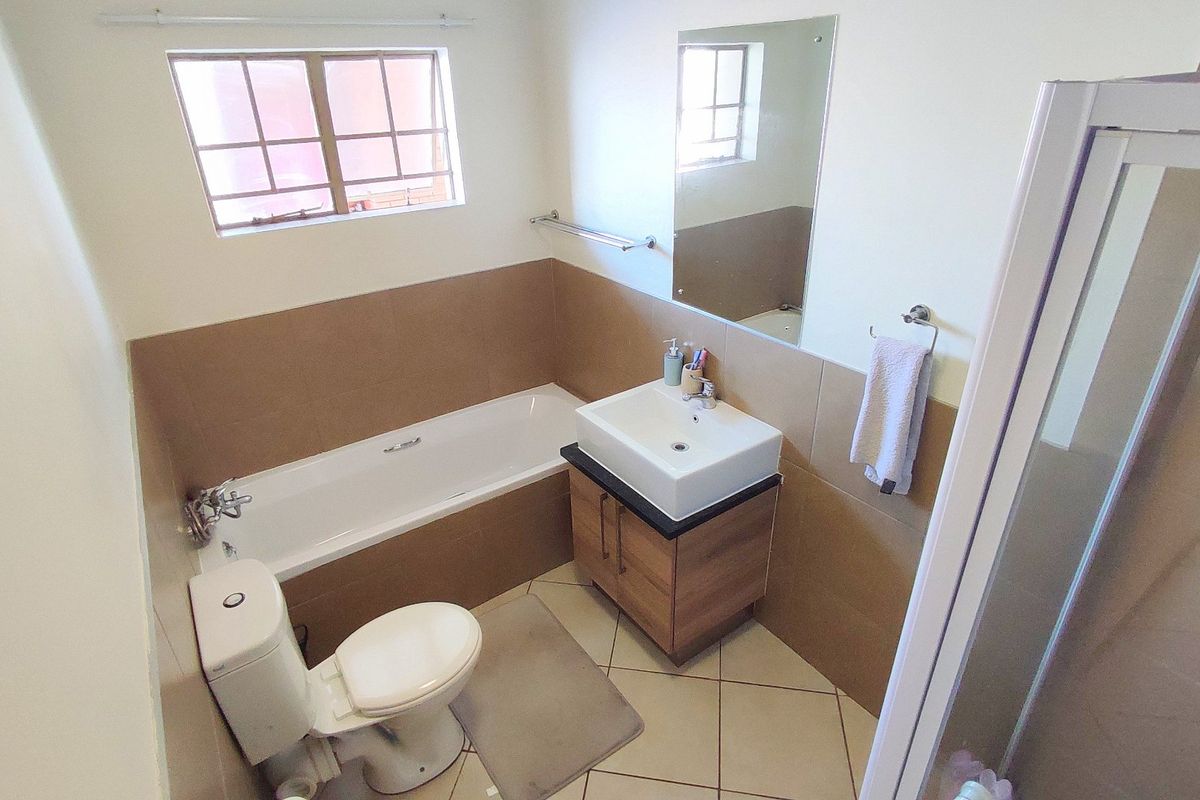 A functional bathroom featuring a bathtub, separate shower enclosure, vanity basin, and neutral wall tiling.