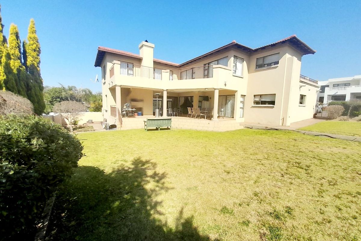 Rear view of the house featuring a spacious lawn, a covered patio area, and an upper-level balcony.