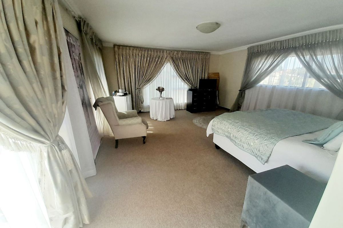 Spacious bedroom featuring neutral carpeting, large windows with layered curtains, and a functional layout suitable for a primary suite.