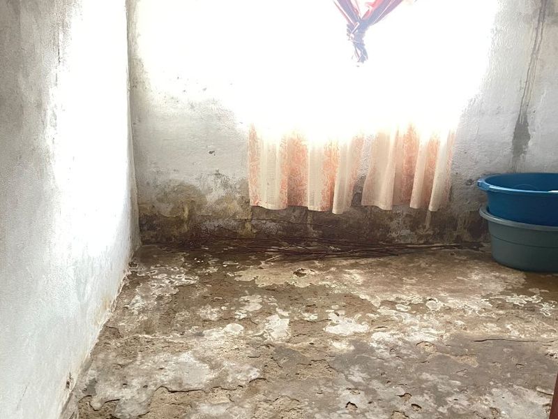 An empty room requiring significant renovation, featuring severely deteriorated concrete flooring and visible damp damage on the lower wall sections.