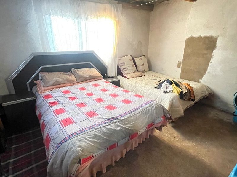 A bedroom featuring an exposed corrugated metal roof, timber rafters, and concrete flooring, requiring significant finishing and renovation to improve the living space.