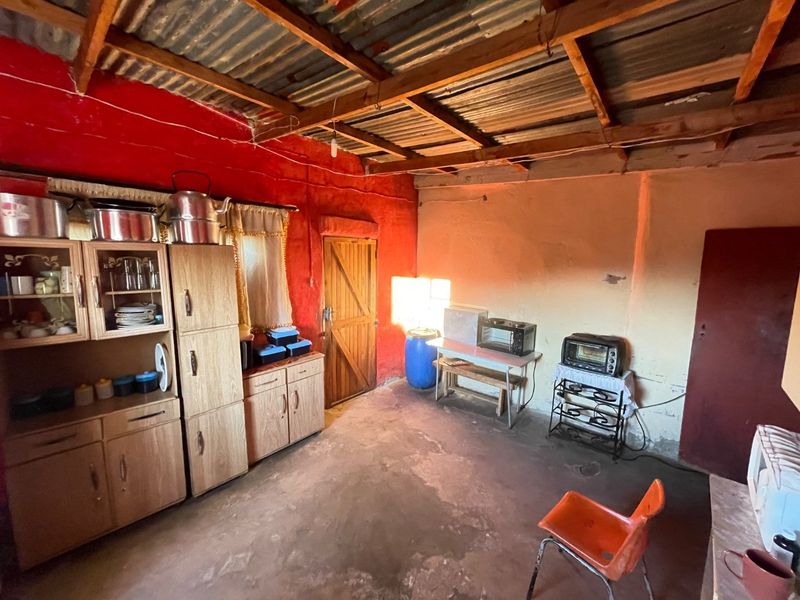 A rustic kitchen area featuring exposed timber roof trusses, corrugated metal ceiling, and concrete flooring, offering a basic functional space with potential for renovation.
