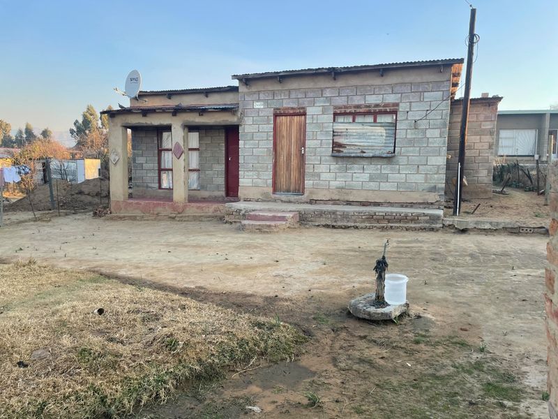 Front elevation of a single-story concrete block house featuring a covered porch, corrugated metal roofing, and an external water connection.