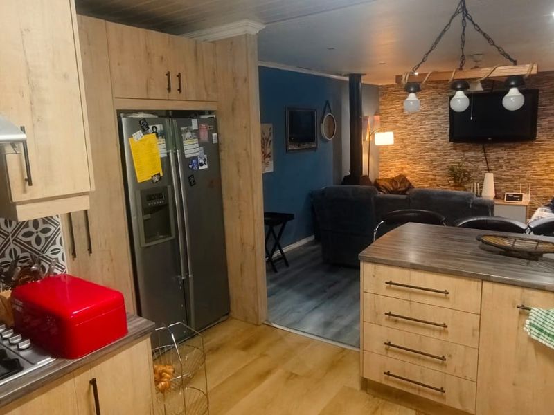 Open-plan kitchen and living area featuring modern wood-look cabinetry, a gas hob, kitchen island, and a cozy living space with a wood-burning stove.