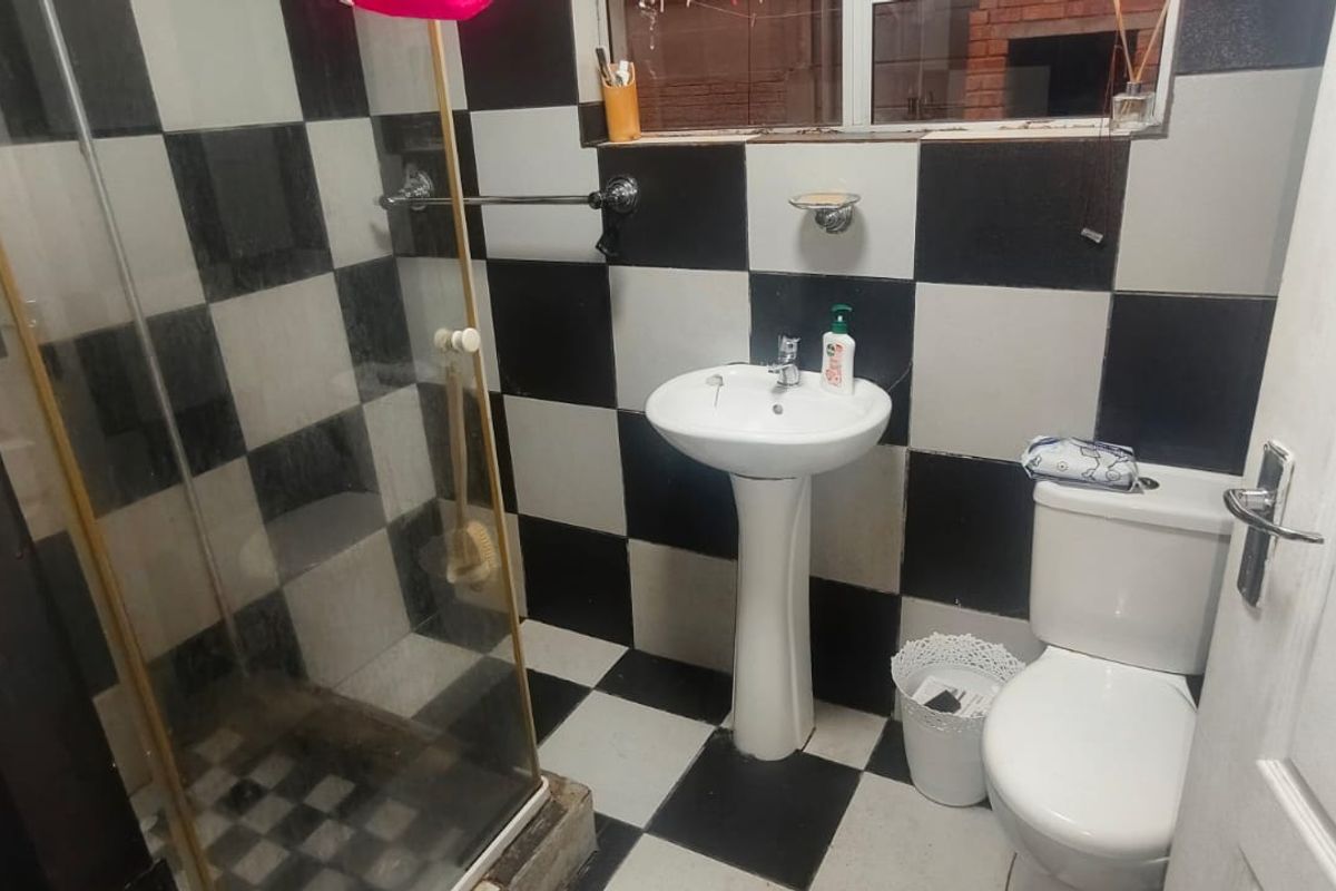 A compact bathroom featuring a pedestal basin, toilet, and shower enclosure with a distinctive black and white checkered tile finish.