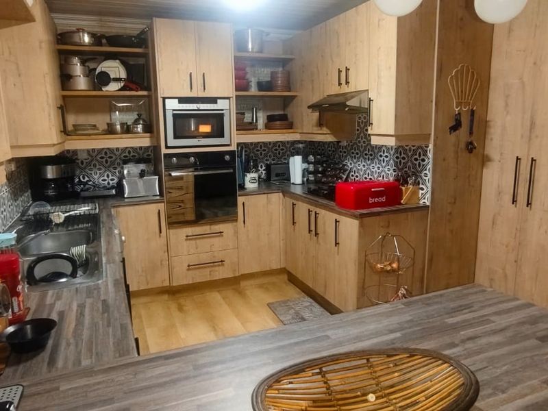 A functional kitchen featuring wood-look cabinetry, patterned tile backsplash, built-in oven and microwave, and ample counter space with a breakfast bar area.
