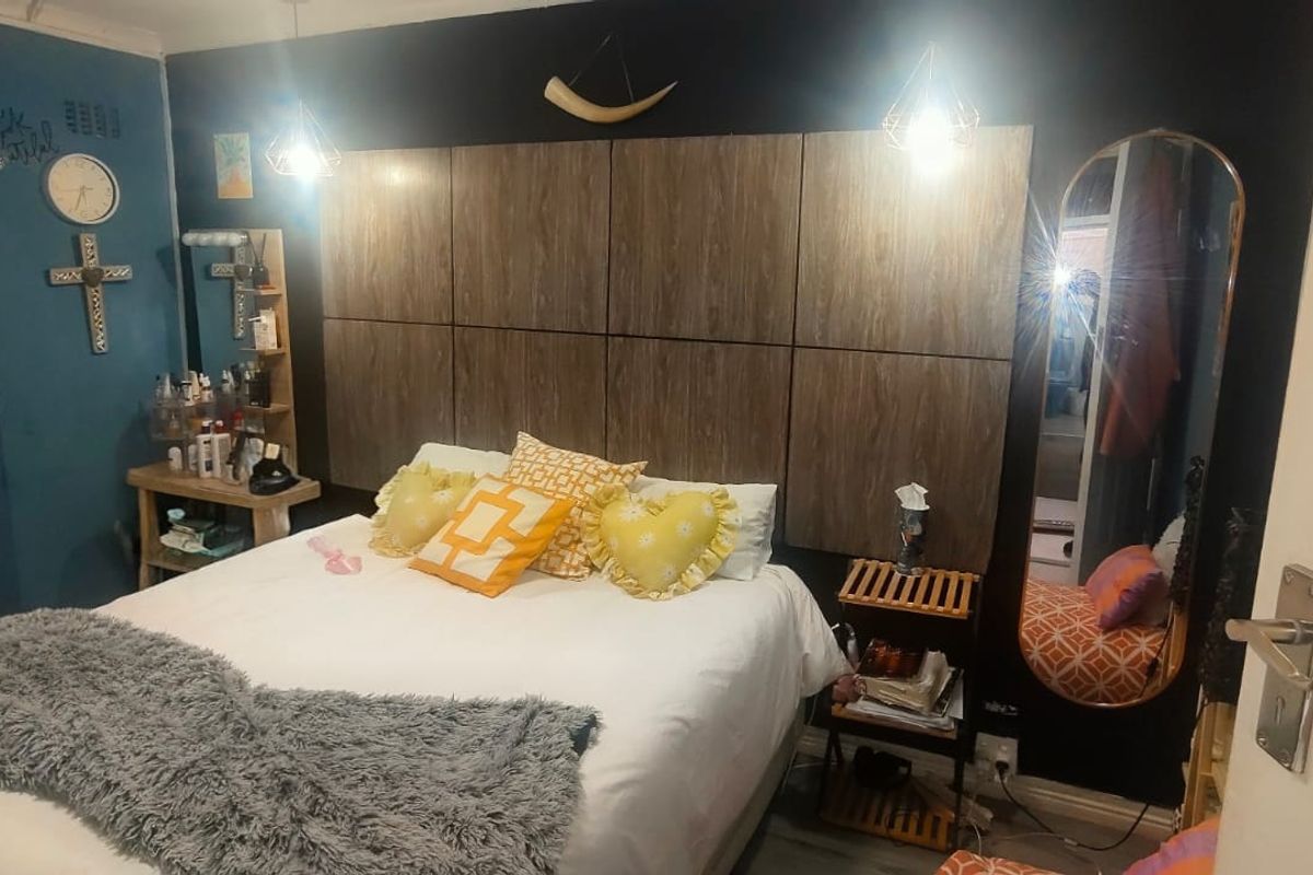 A bedroom featuring a large wood-panelled built-in headboard and pendant lighting, with dark accent walls.
