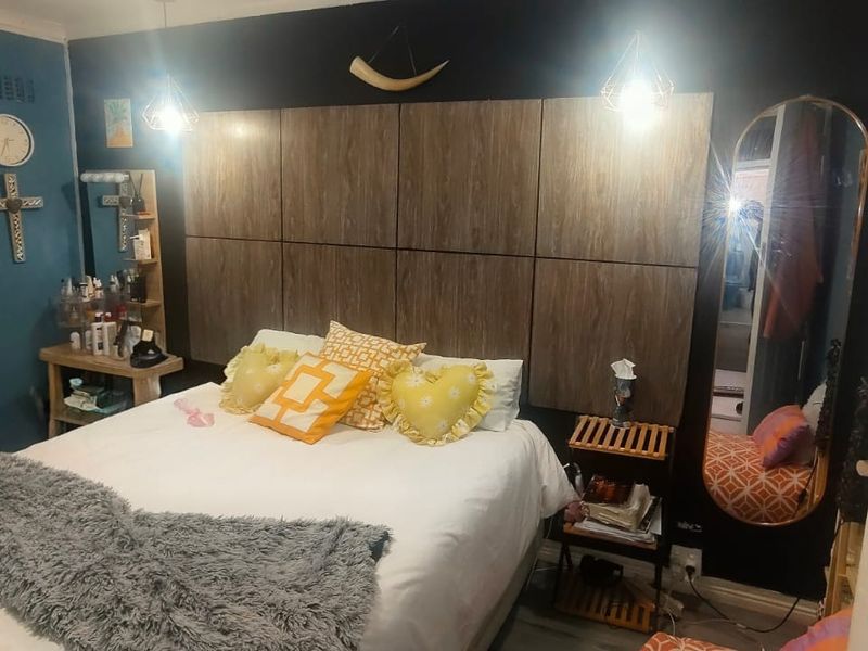 A bedroom featuring a large wood-panelled built-in headboard and pendant lighting, with dark accent walls.