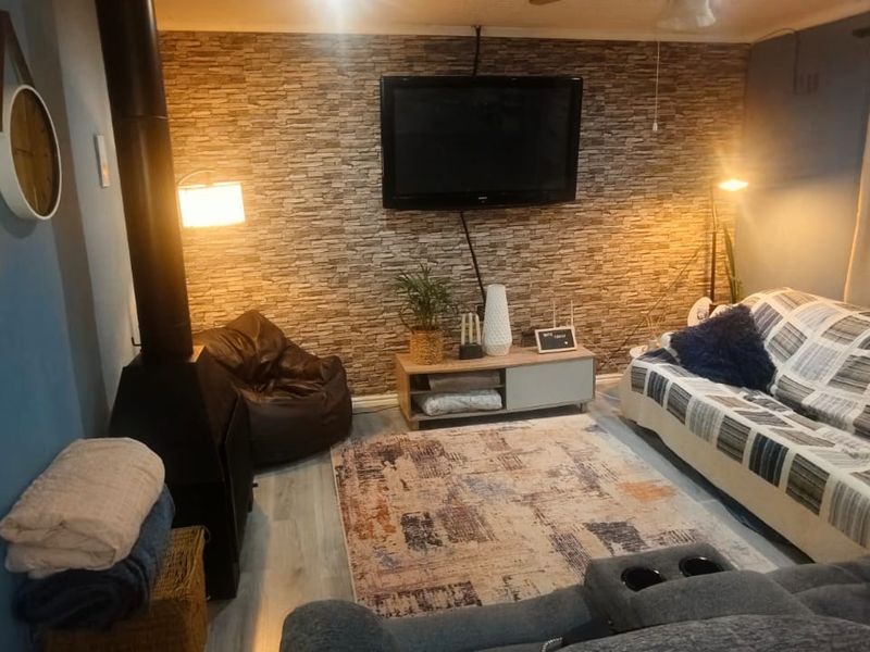 A cozy living room featuring a stone-cladding accent wall, a freestanding fireplace, and modern laminate flooring.